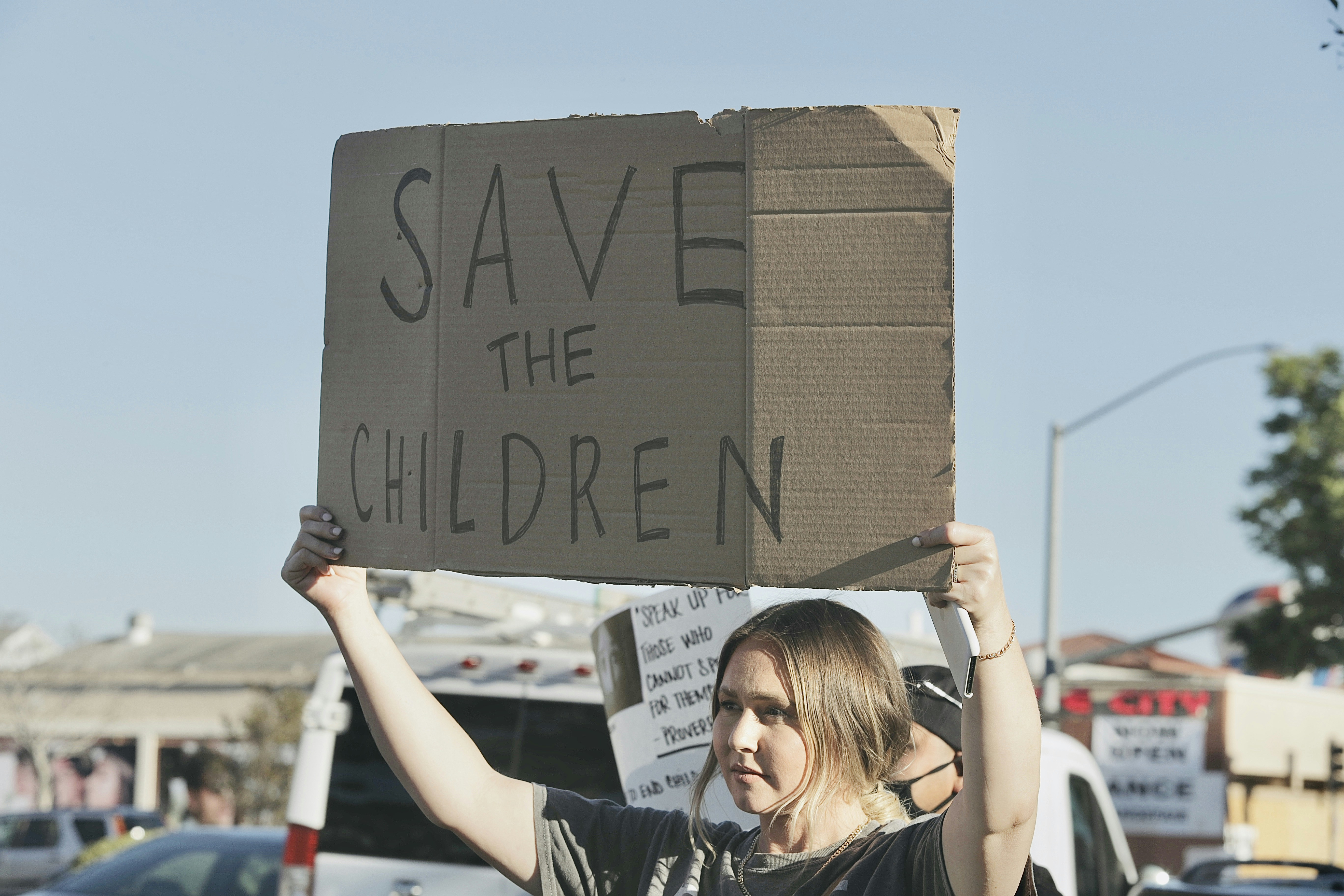 Woman at a demo holding a sign saying "Save the children"