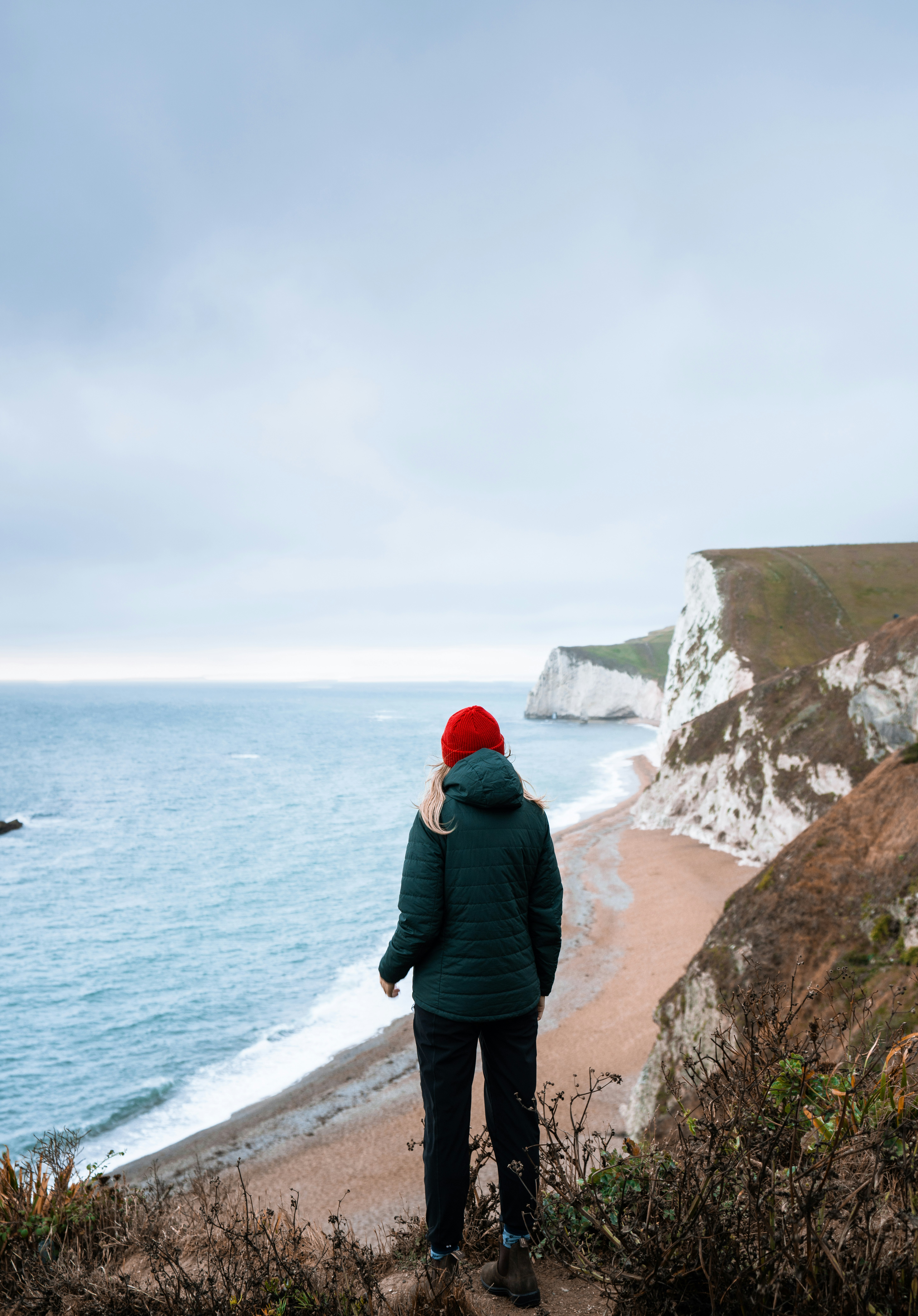 woman in green hoodie standing on brown rock formation near body of water during daytime