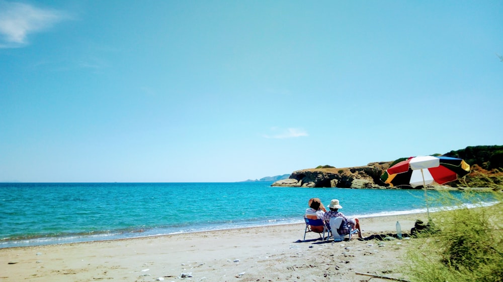 man and woman sitting on beach shore during daytime