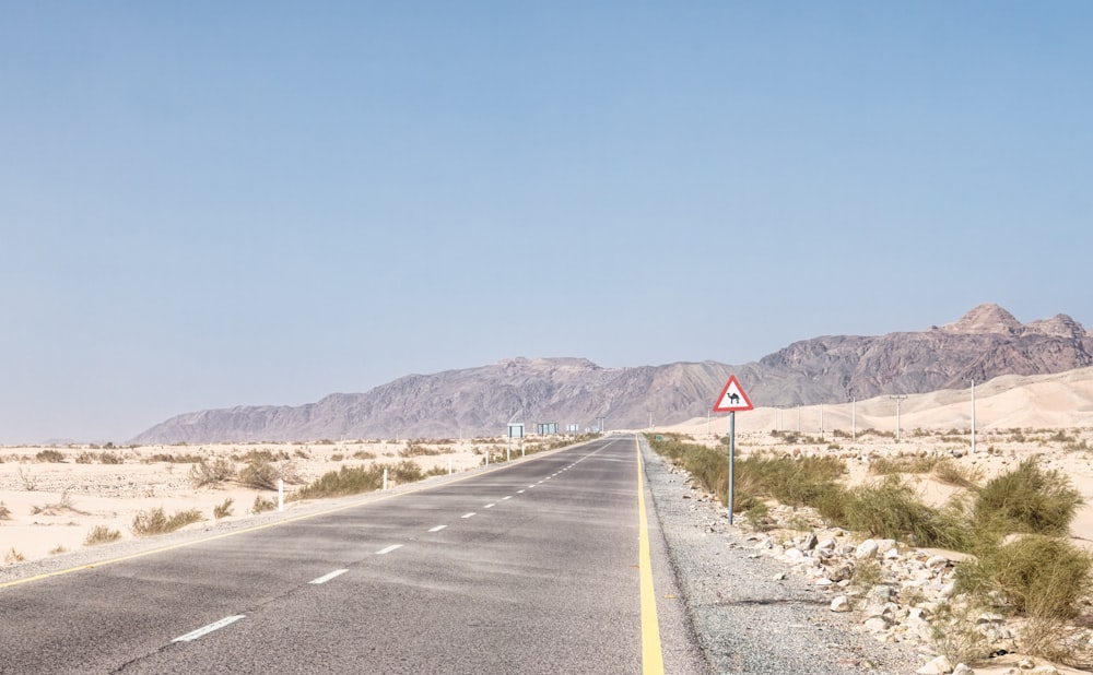 gray concrete road near mountain under blue sky during daytime