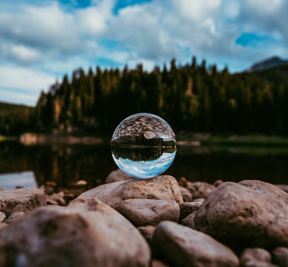 clear glass ball on gray rock near body of water during daytime