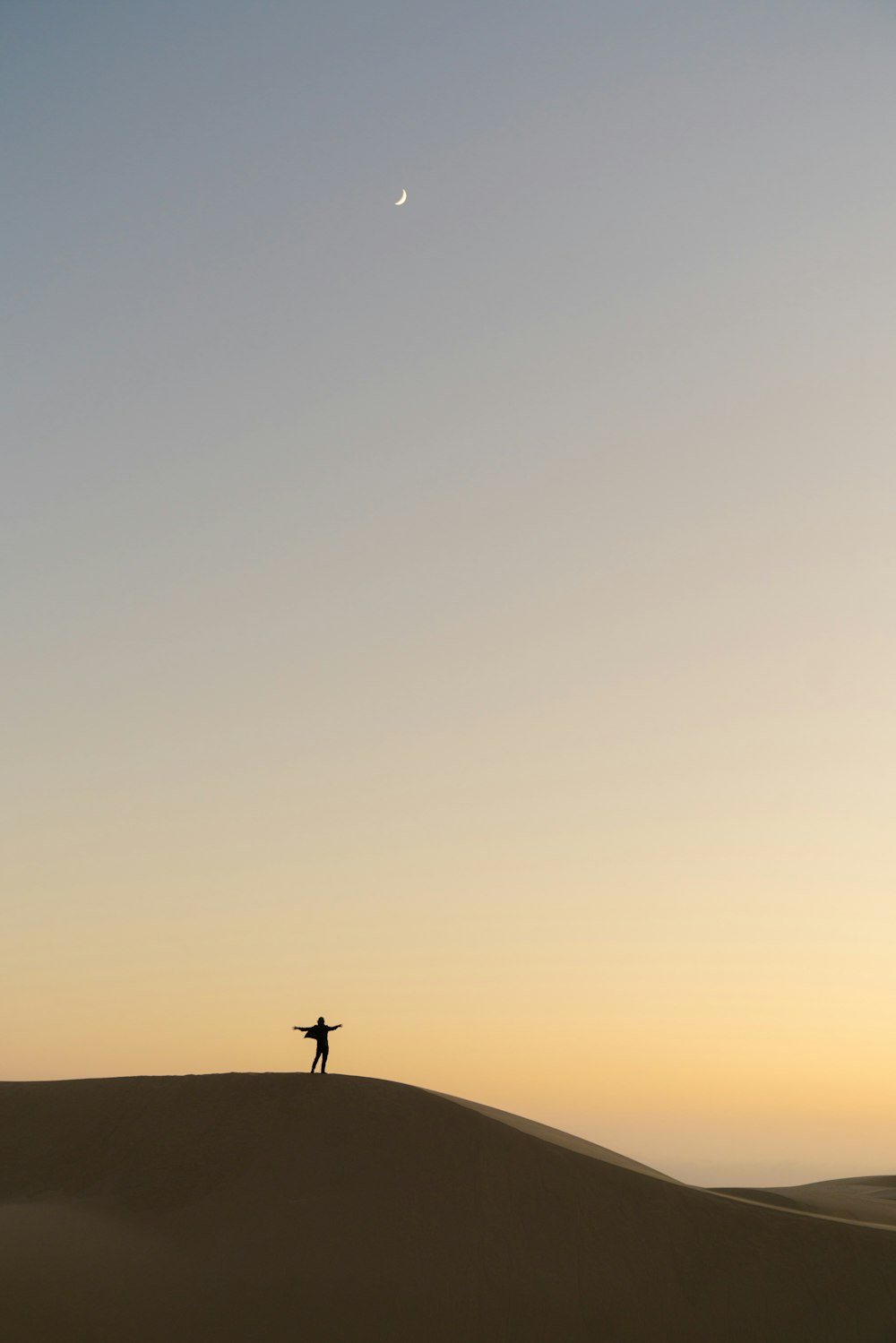 silhueta do homem em pé na areia durante o pôr do sol