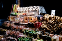 A display of assorted sweets, including gingerbread cookies decorated with icing, panda-shaped lollipops, licorice sticks, and pretzels. The items are arranged on shelves, with some wrapped in clear packaging. The scene has a festive and colorful atmosphere highlighted by a dark background.