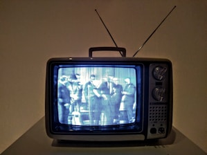 A vintage television set displaying a black and white image of several people gathered together. The TV has a boxy design with dials and an antenna on top.