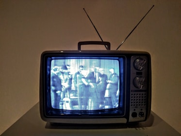 A vintage television set displaying a black and white image of several people gathered together. The TV has a boxy design with dials and an antenna on top.