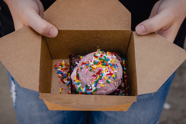 A cheerful delivery person handing over a box of assorted ice cream and beverages at a customer's doorstep.