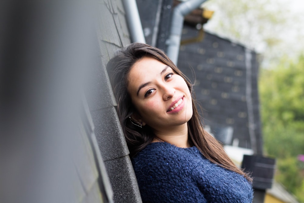 woman in blue sweater leaning on gray wall