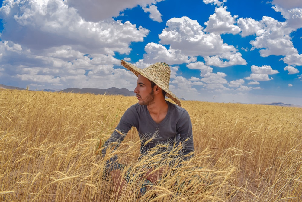 man in brown hat and gray jacket on brown grass field under blue and white cloudy