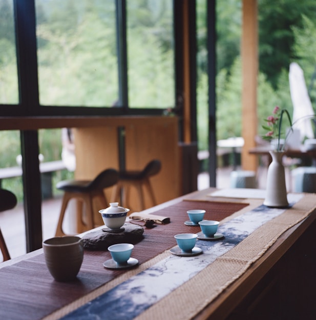 A beautifully arranged tea set with delicate porcelain cups and a teapot on a rustic wooden table bathed in soft natural light.