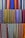 A collection of colorful woven fabrics is neatly arranged in rows. The fabrics feature various patterns, including stripes and geometric designs, with a vibrant range of colors including reds, blues, yellows, and purples. Each fabric has a unique pattern and color combination, creating a visually rich tapestry.