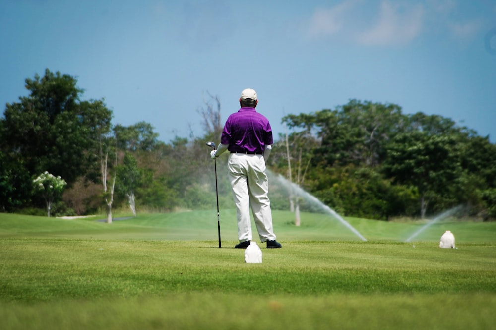 uomo in giacca viola e pantaloni bianchi che gioca a golf durante il giorno