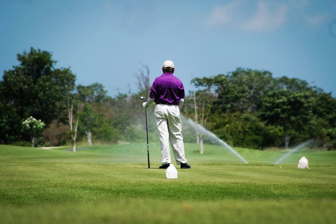 man in purple jacket and white pants playing golf during daytime,