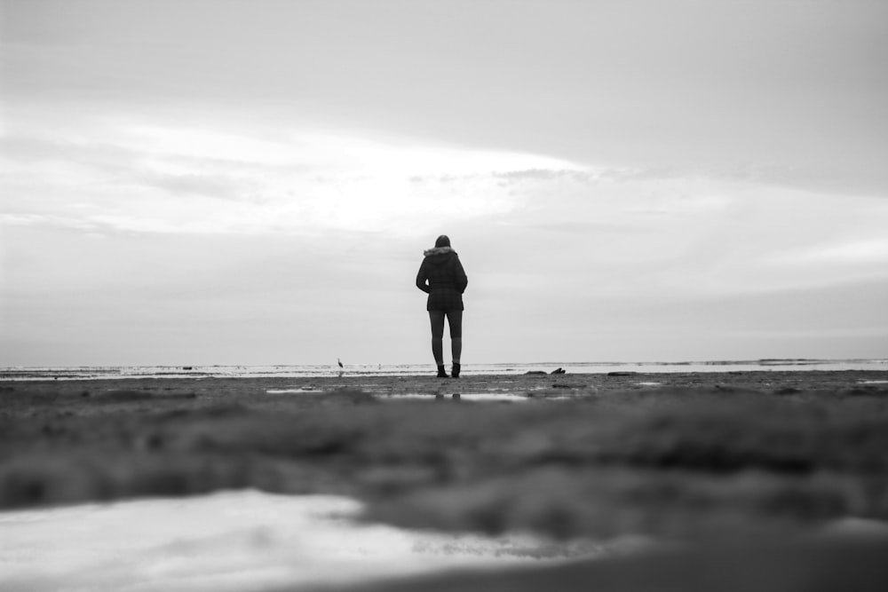 grayscale photo of person standing on seashore
