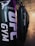 A row of black punching bags hangs in a gym, with clear branding on the front. The gym has an industrial vibe with exposed ceilings and a mix of artificial lighting adding purplish and yellowish hues.