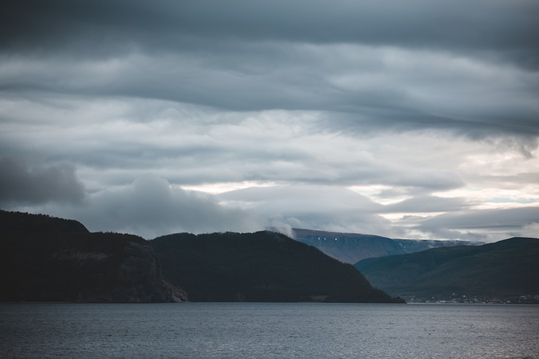 body of water near mountain under cloudy sky during daytime