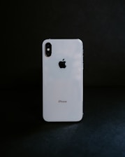 A white smartphone with a reflective surface stands against a dark background, displaying the Apple logo prominently.