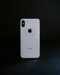 A white smartphone with a reflective surface stands against a dark background, displaying the Apple logo prominently.