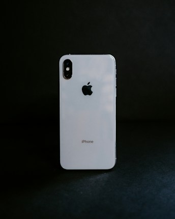 A white smartphone with a reflective surface stands against a dark background, displaying the Apple logo prominently.
