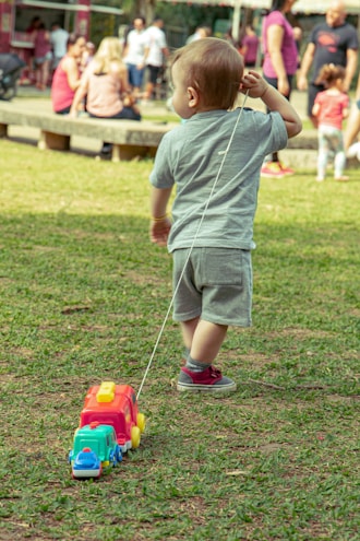 boy in grey t-shirt and grey shorts playing with red and yellow toy car on on on on on