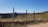 A rural landscape featuring sturdy fiberglass posts supporting a wire fence under a clear blue sky.