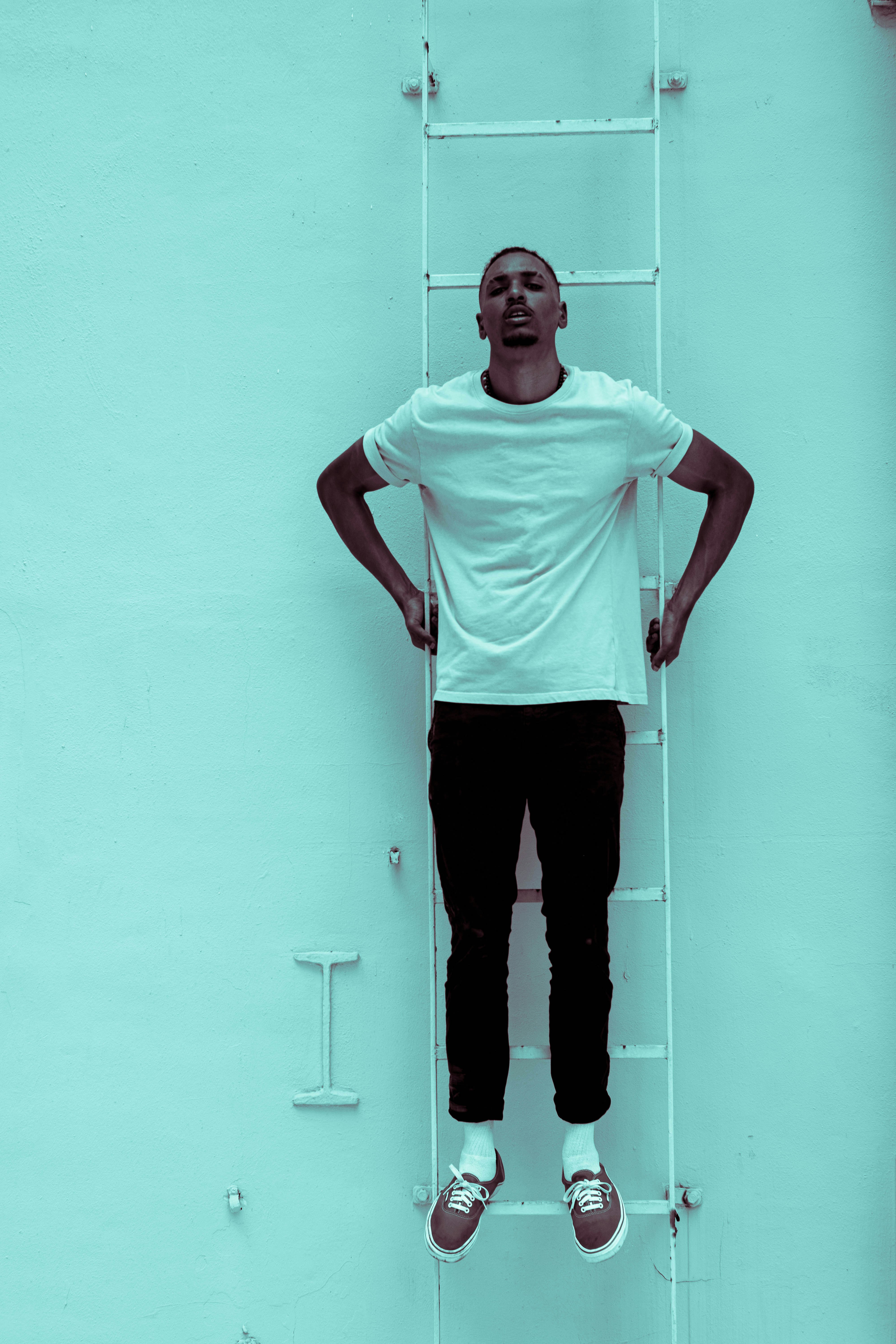 man in white crew neck t-shirt and black pants standing beside white wall