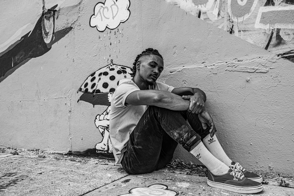 grayscale photo of boy in t-shirt leaning on wall