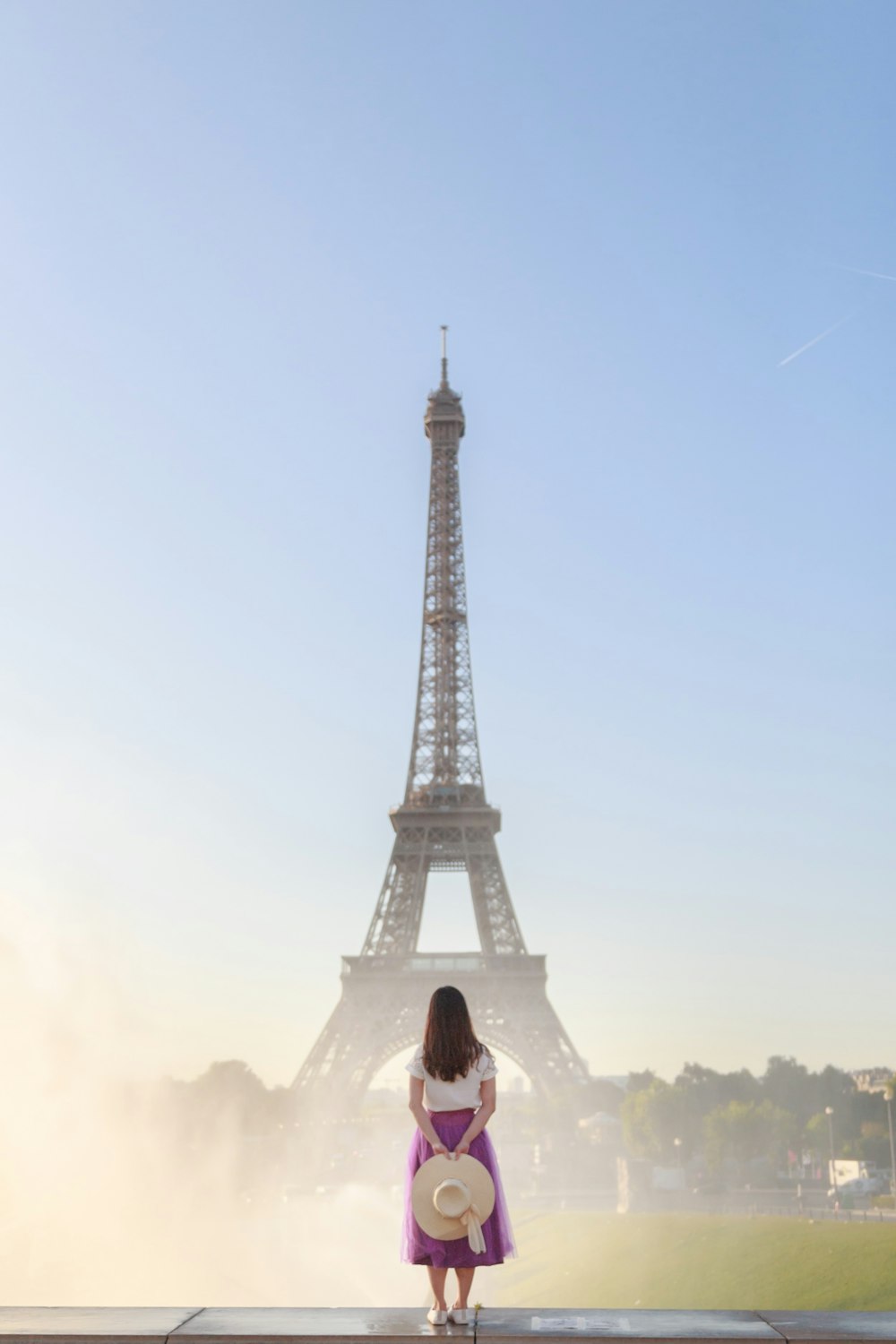 woman in white shirt sitting on the ground near eiffel tower during daytime