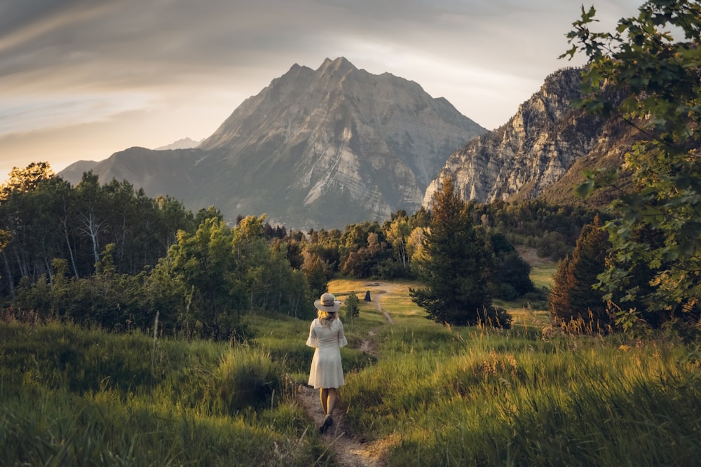 person in white shirt standing on green grass field near mountain during daytime