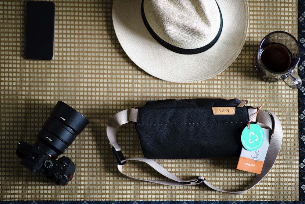 black dslr camera beside black leather sling bag and white fedora hat