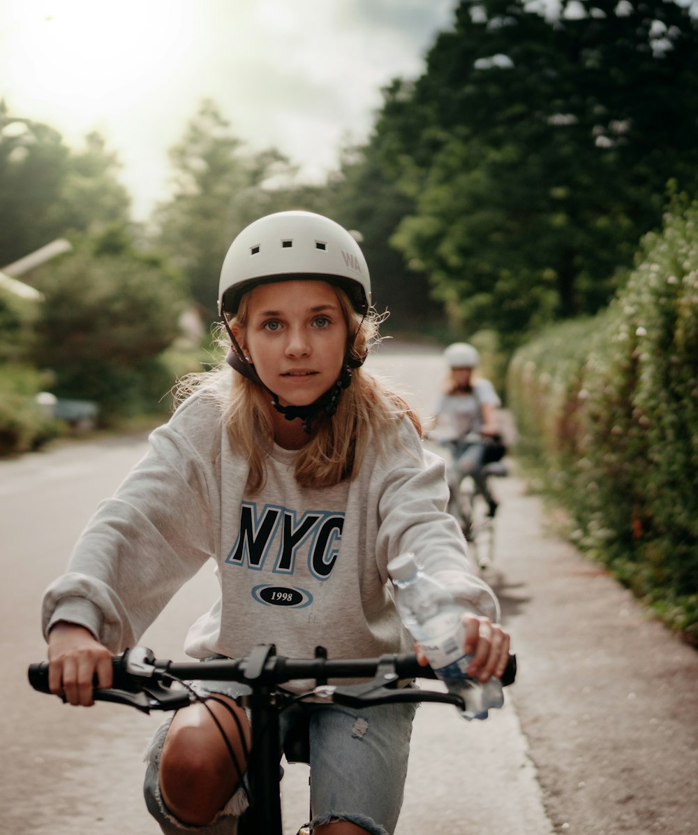 donna in camicia bianca a maniche lunghe in sella alla bicicletta su strada durante il giorno