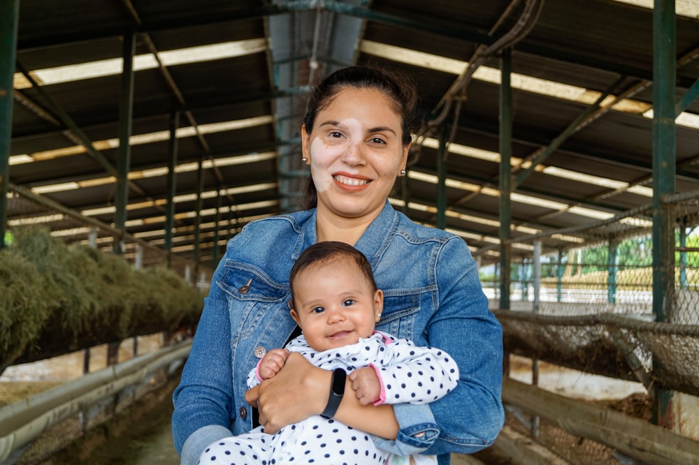 smiling woman in blue denim jacket carrying baby in white and black polka dot dress