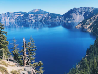 A natural blue mountain lake reflecting the surrounding dark gray cliffs and pine trees.