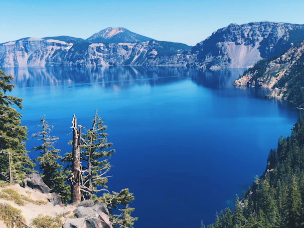 A natural blue mountain lake reflecting the surrounding dark gray cliffs and pine trees.