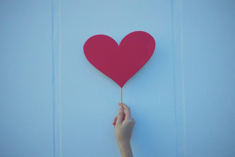 person holding heart shaped red balloon