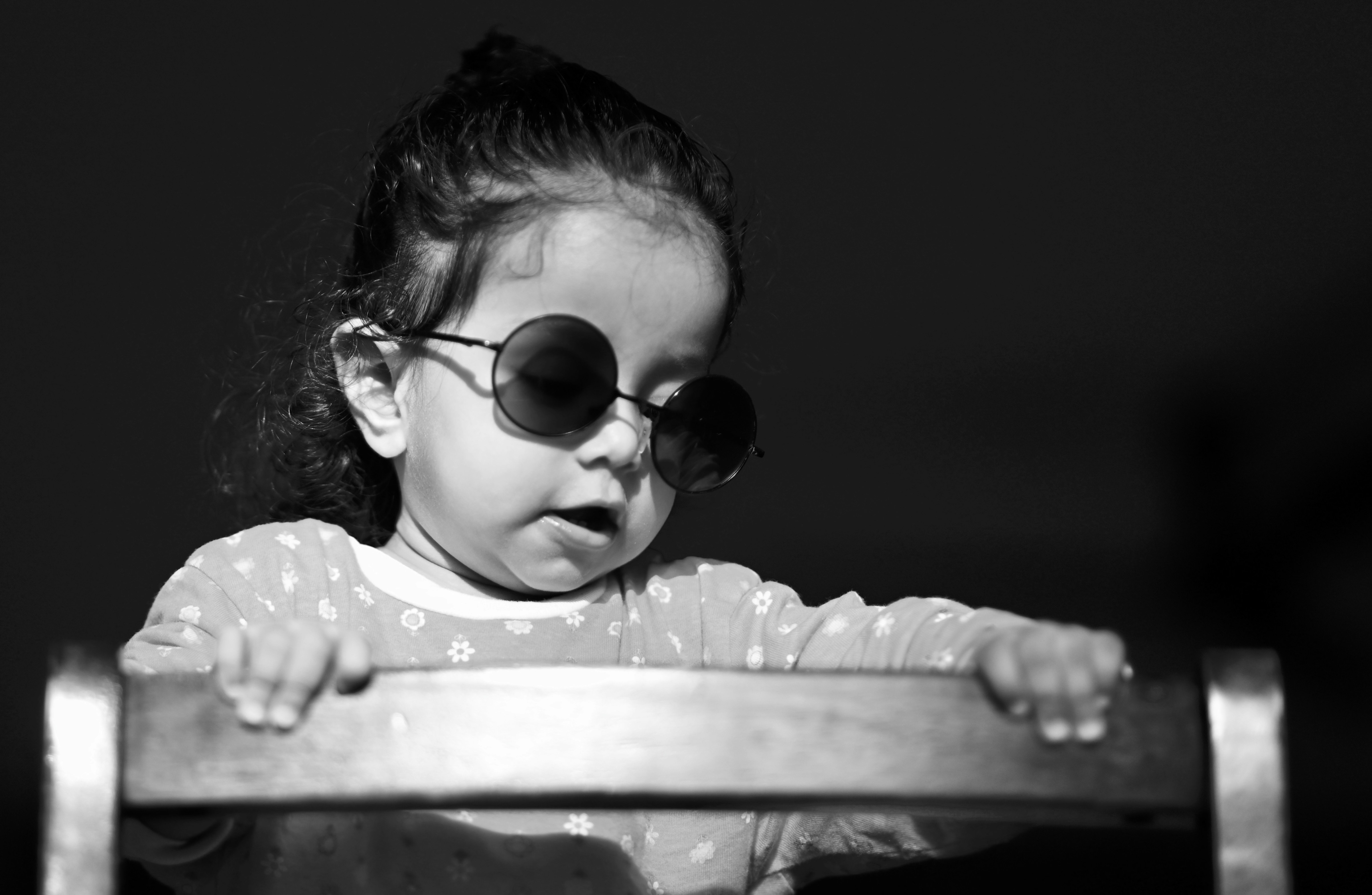 a little girl wearing sunglasses looking over a chair