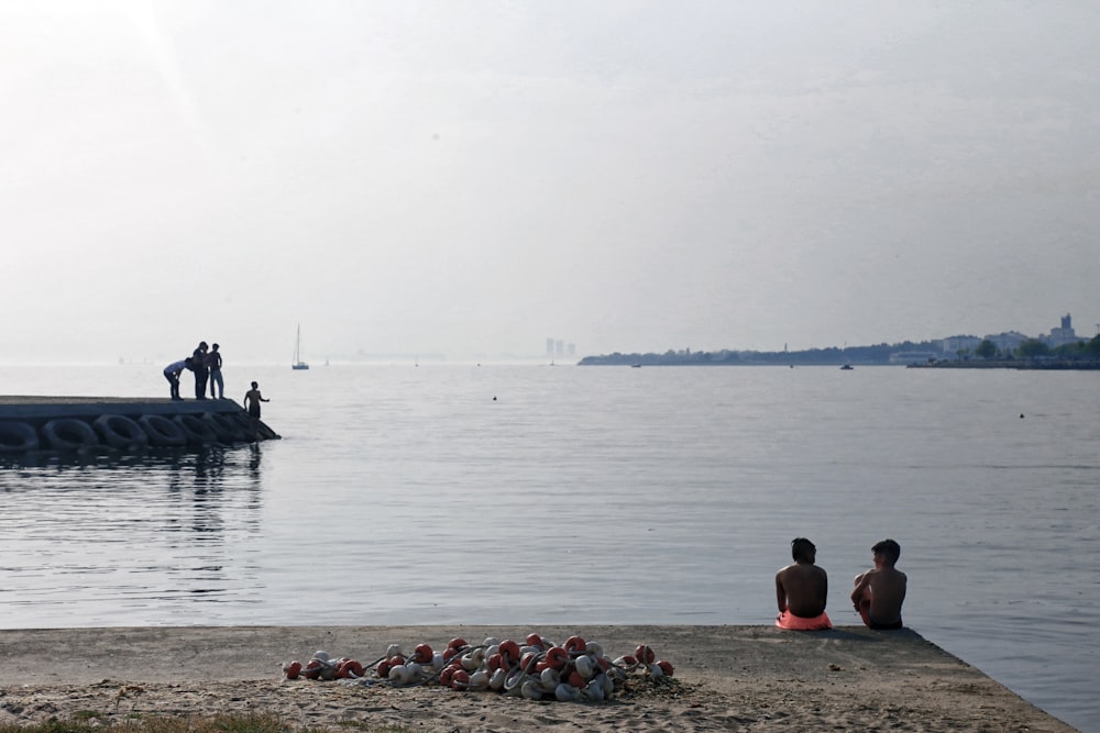 personas sentadas en la roca cerca del cuerpo de agua durante el día