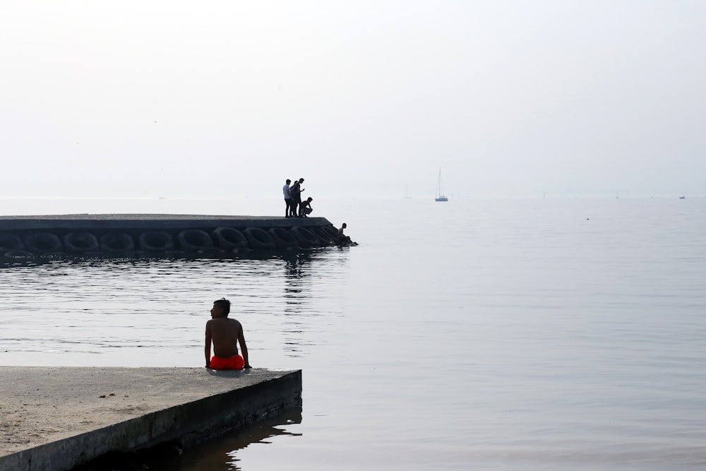 woman in pink shirt sitting on concrete dock during daytime