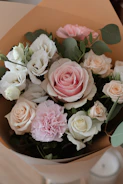A lush bouquet of soft pastel flowers including roses and eucalyptus, wrapped in simple kraft paper.