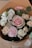 A bouquet of flowers featuring a variety of blooms, including pastel pink and white roses, a pink carnation, and white lisianthus. The flowers are accompanied by green leaves and are wrapped in brown paper.