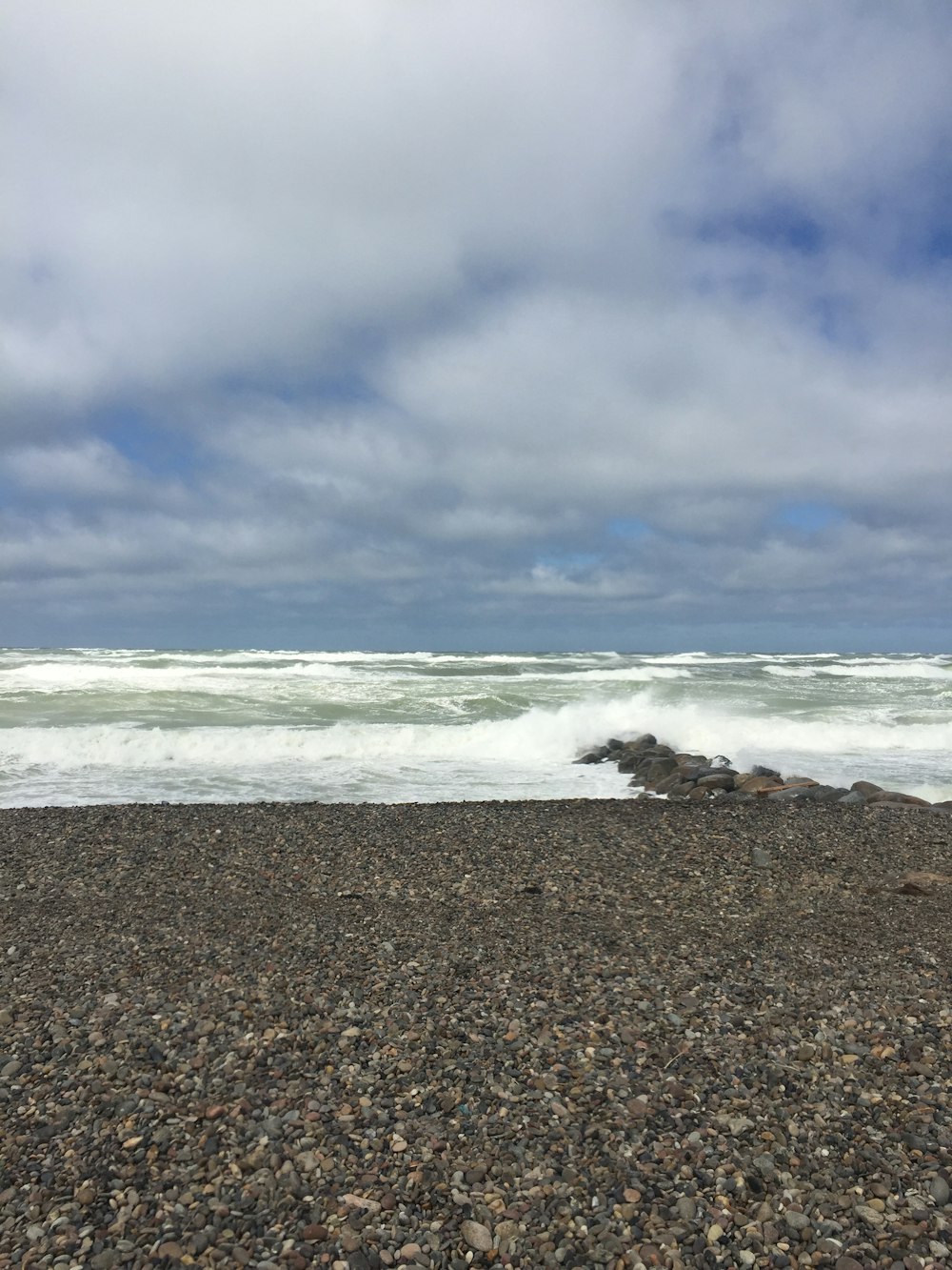 ocean waves crashing on shore under cloudy sky during daytime