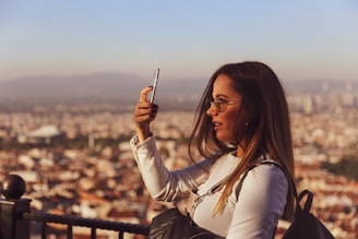Close-up of a smiling woman holding a phone, with a blurred city background.