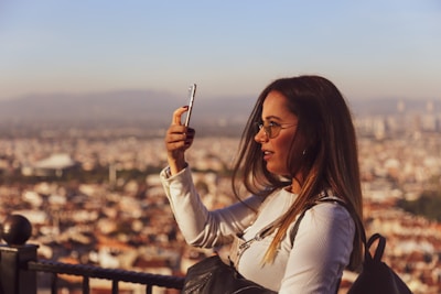 A candid snapshot of a smiling woman holding her phone, with a blurred city background.