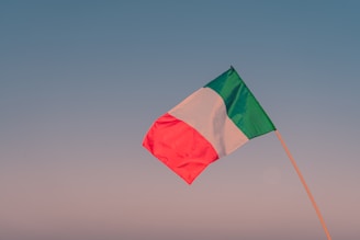 The Italian flag waving gently against a bright blue sky over farmland.