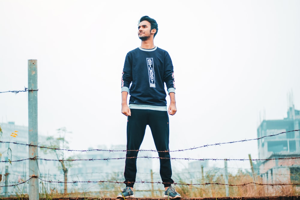 man in black and gray sweater standing near fence