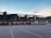 A large, iconic sports stadium with the Green Bay Packers logo prominently displayed, surrounded by an empty parking lot. The stadium is constructed with green and brown elements, and the sky above is partly cloudy with soft evening light.