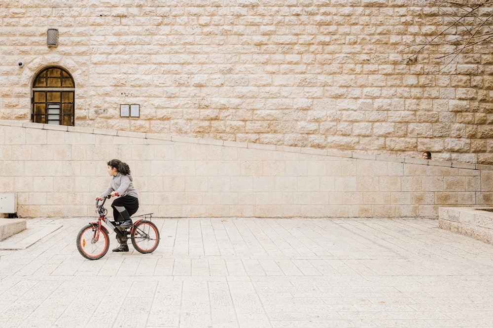 낮 동안 벽돌 벽 근처에서 자전거를 타고 있는 검은 재킷을 입은 여자