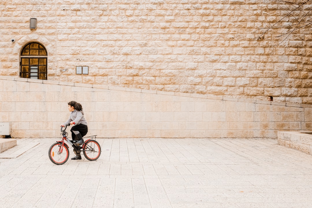 woman in black jacket riding on bicycle near brick wall during daytime