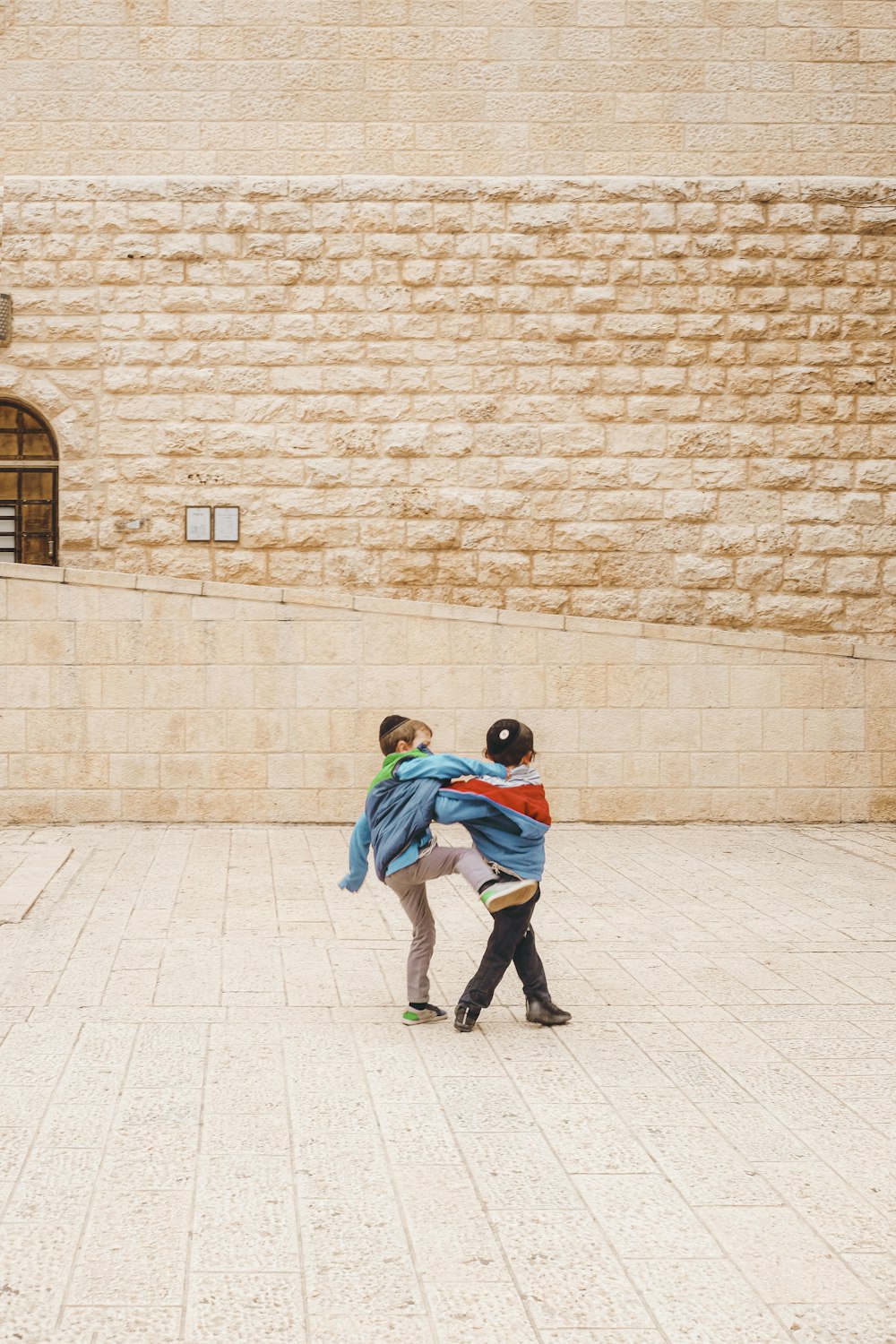 2 boys in green and blue jacket walking on gray concrete floor during daytime