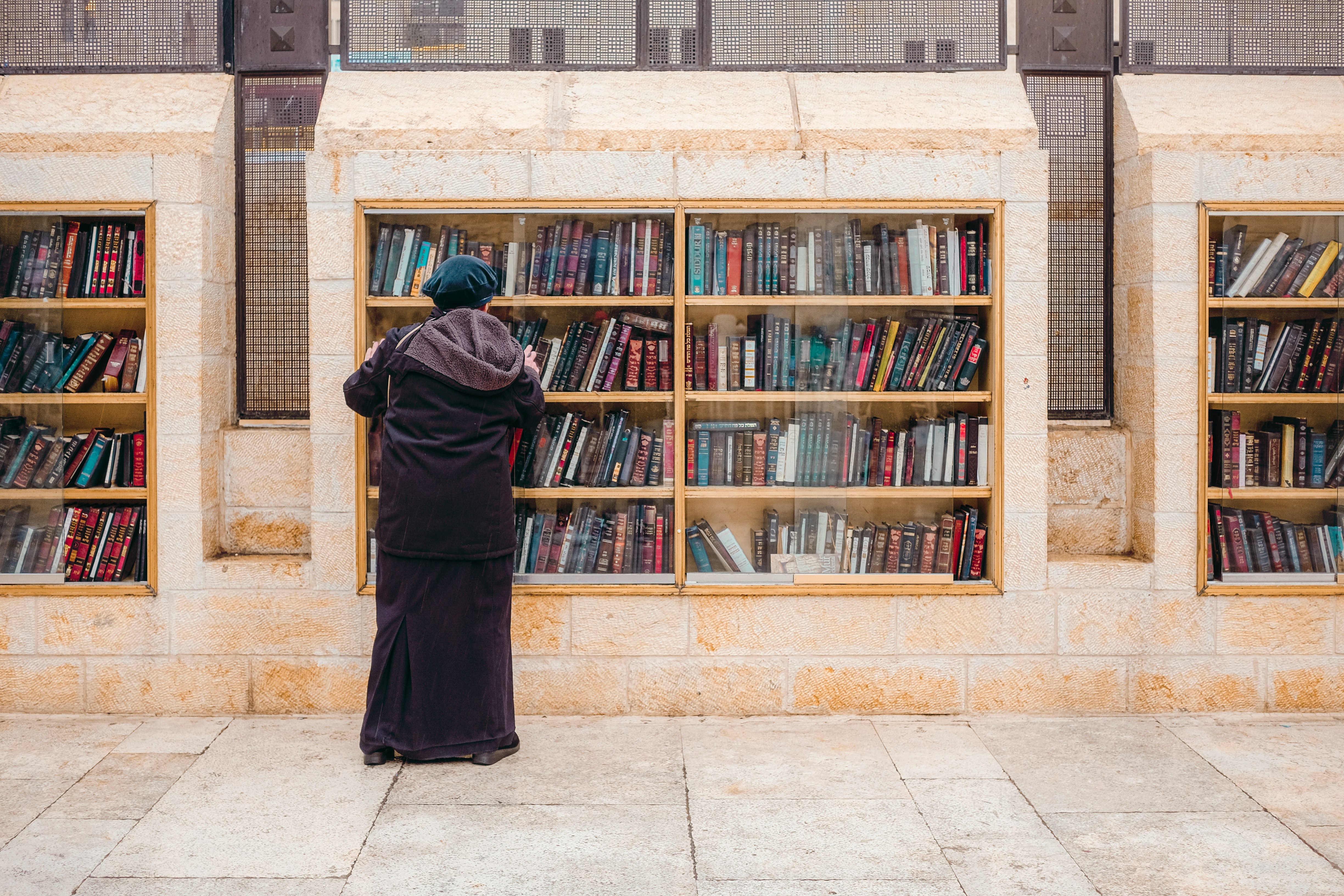 man in black robe standing near brown wooden book shelf