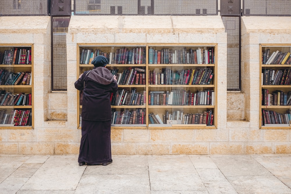 man in black robe standing near brown wooden book shelf